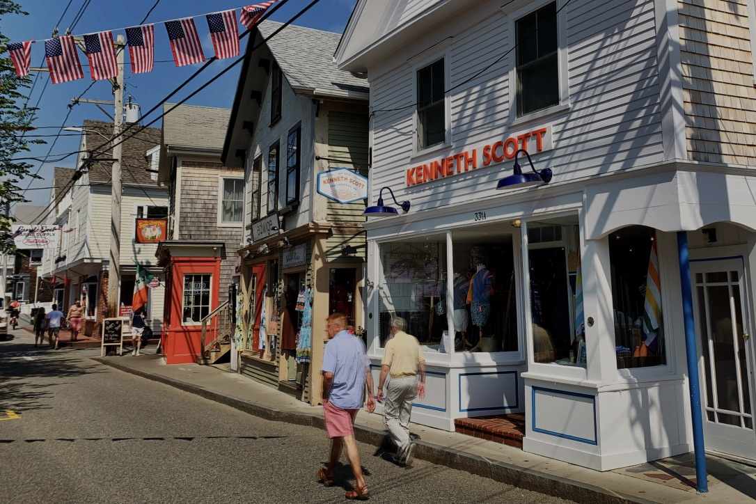 shot people walking on Commercial Street. Steet is flanked with 1850s houses in different colors with storefronts and US flags hanging on across the street