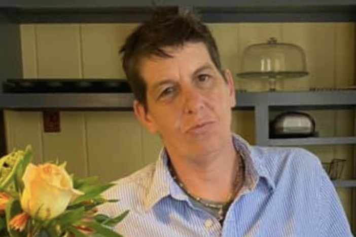 portrait of woman with short dark hair in a light blue blouse, standing next to a flour arrangement with yellow roses